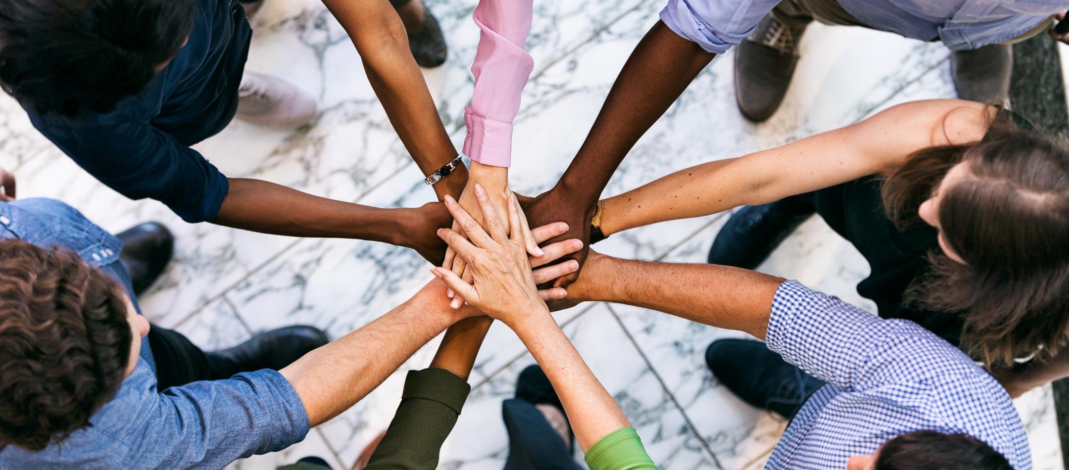 Aerial photo of a team of people with hands overlapping in the middle